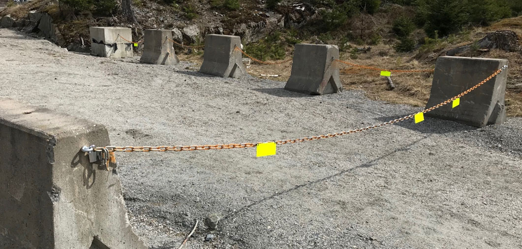 Sperrebukker ved en grusvei. En kjetting henger i mellom to av dem for å sperre gjennomkjørsel.